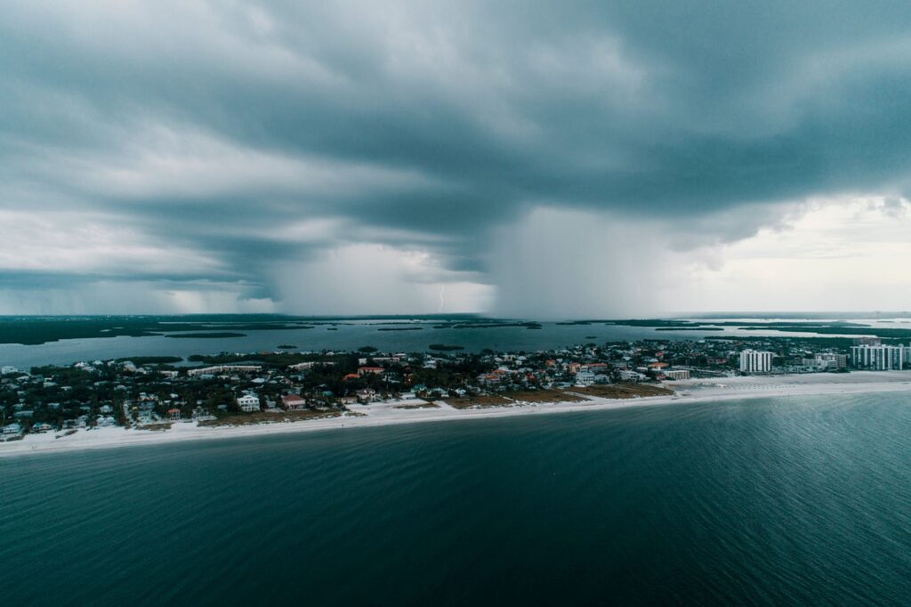 Aerial view of a rain squall and dark storm clouds approaching a coastal town and white-sand beach