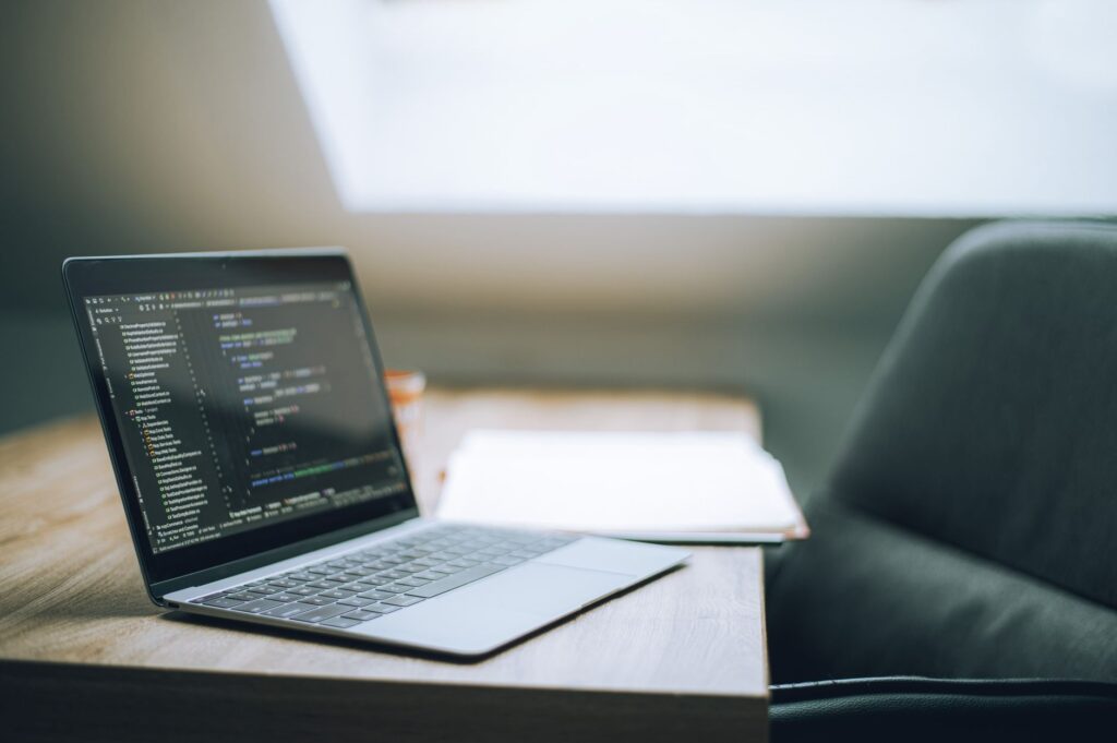 Open laptop displaying lines of code on a desk beside a chair in soft daylight
