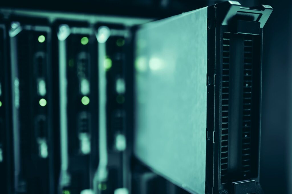 Close-up of server drive bays with glowing green status lights in a dark teal data center rack, shallow depth of field