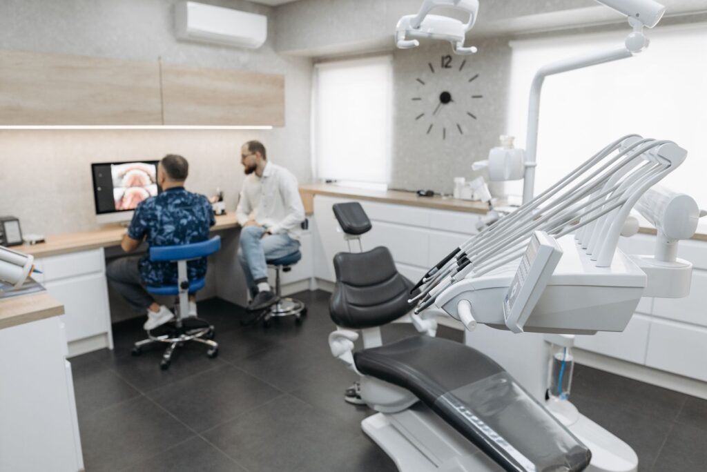 Dental exam room with a treatment chair and two people seated at a desk looking at a computer monitor
